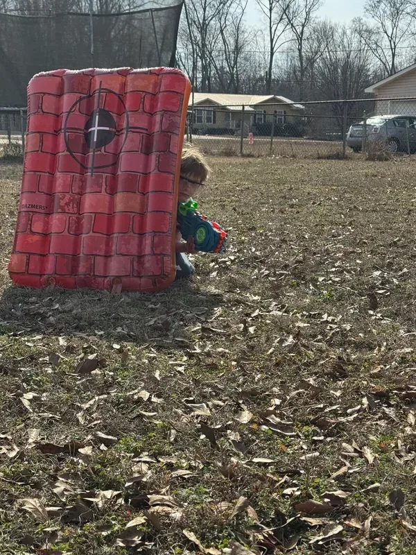 Child crouching behind an inflatable barrier with a Nerf blaster